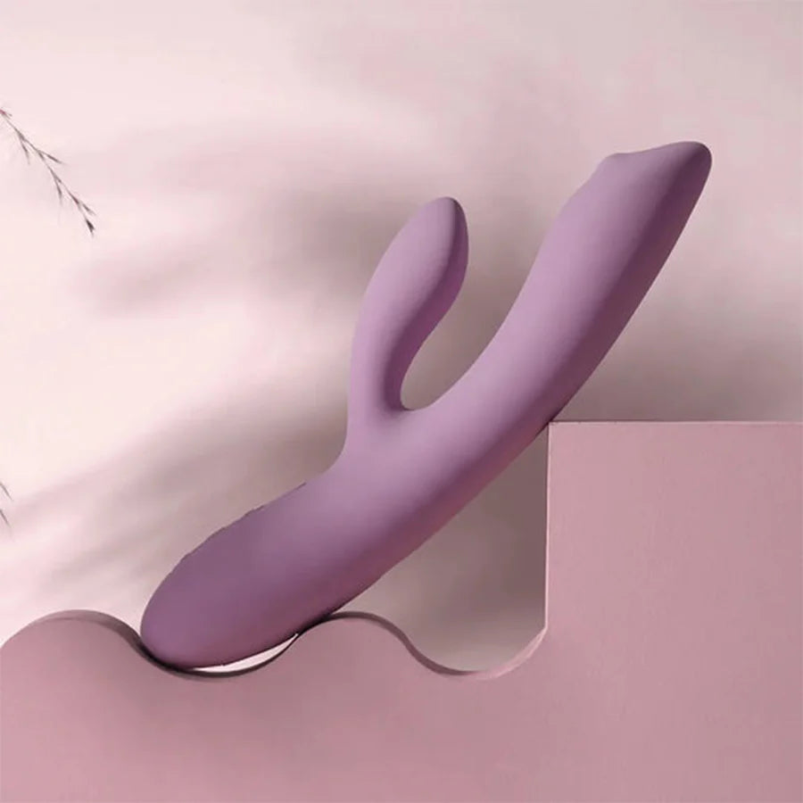 Vibrador Trysta NEO lila sobre base rosada, diseño ergonómico para doble estimulación de punto G y clítoris.